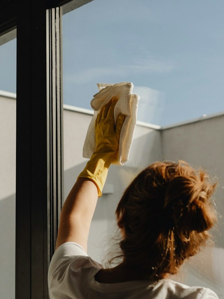 Eine Person in gelben Handschuhen säubert ein Fenster mit einem Tuch.